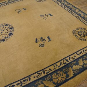 Tan and navy rug featuring sparse medallions and complex floral borders rests on wood flooring.