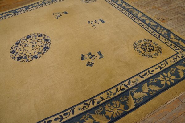 Tan and navy rug featuring sparse medallions and complex floral borders rests on wood flooring.