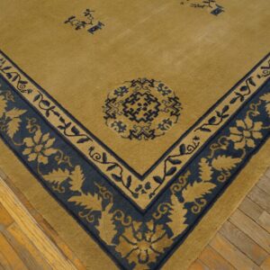 Low-pile gold rug corner with a navy blue border featuring stylized foliage and geometric patterns on wood flooring.