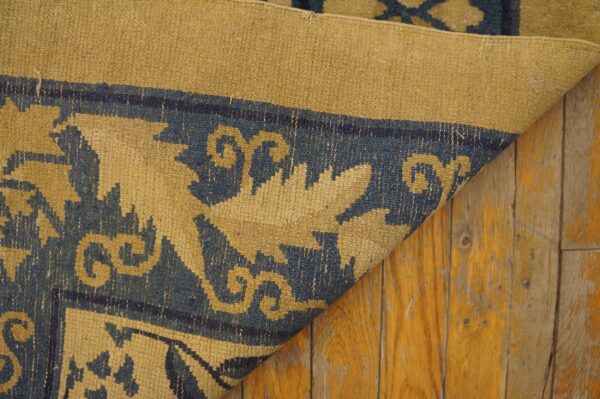 Low-pile blue and tan rug showing a detailed foliage pattern, folded over rustic amber wood planks.