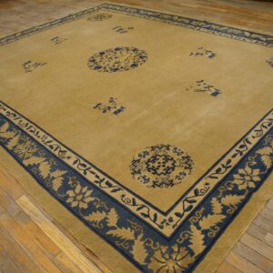 Gold and navy blue rug featuring a wide floral border displayed on rustic wood plank flooring.