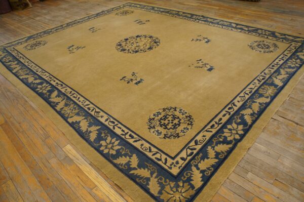 Gold and navy blue rug featuring a wide floral border displayed on rustic wood plank flooring.