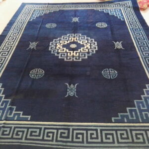 Dark indigo rug featuring a pale blue Greek key border and central geometric motifs on a light tile floor.