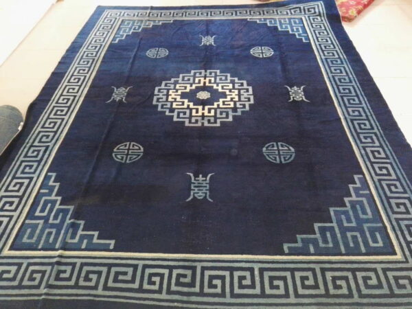 Dark indigo rug featuring a pale blue greek key border and central geometric motifs on a light tile floor.