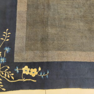 Gray and taupe distressed rug corner with a navy blue border featuring yellow and blue flowers.