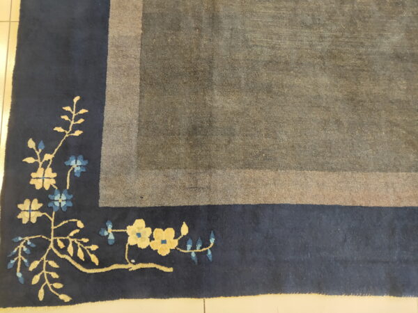 Gray and taupe distressed rug corner with a navy blue border featuring yellow and blue flowers.