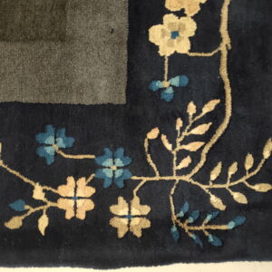 Close-up of a navy rug border featuring carved beige and blue floral vines next to a striped gray field.