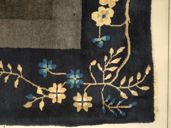 Close-up of a navy rug border featuring carved beige and blue floral vines next to a striped gray field.