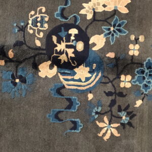 Dark gray rug detail with sculpted blue and peach floral motifs surrounding a central navy medallion.