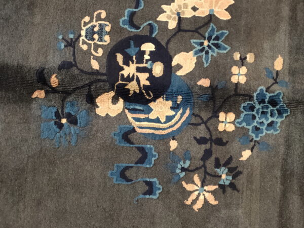 Dark gray rug detail with sculpted blue and peach floral motifs surrounding a central navy medallion.