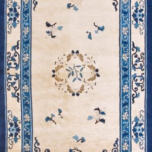 Beige rug with navy and light blue scrolling floral borders shown on a distressed wood floor.