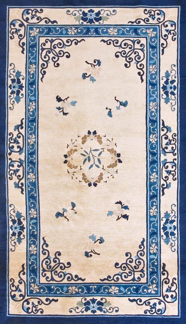 Beige rug with navy and light blue scrolling floral borders shown on a distressed wood floor.