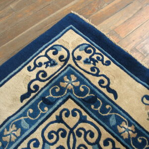 High-pile rug corner featuring navy, light blue, and beige scrolling patterns on distressed plank flooring.