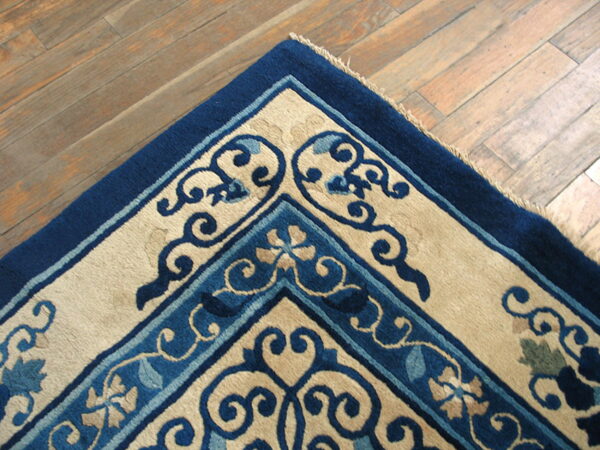 High-pile rug corner featuring navy, light blue, and beige scrolling patterns on distressed plank flooring.