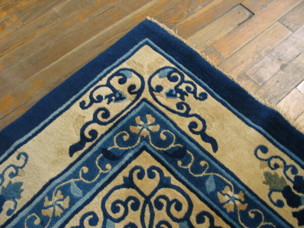 Blue and tan rug corner featuring scrolling floral motifs against distressed wood flooring.