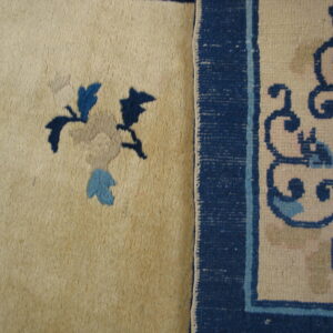 Creamy high pile rug detail features dark blue floral elements next to a dark blue woven border with scroll patterns.