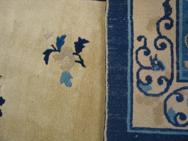 Creamy high pile rug detail features dark blue floral elements next to a dark blue woven border with scroll patterns.