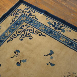Close-up of a tan rug with dark blue floral borders against distressed brown hardwood flooring.