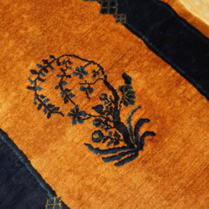 Orange rug with navy blue floral pattern and borders resting on light wood flooring.