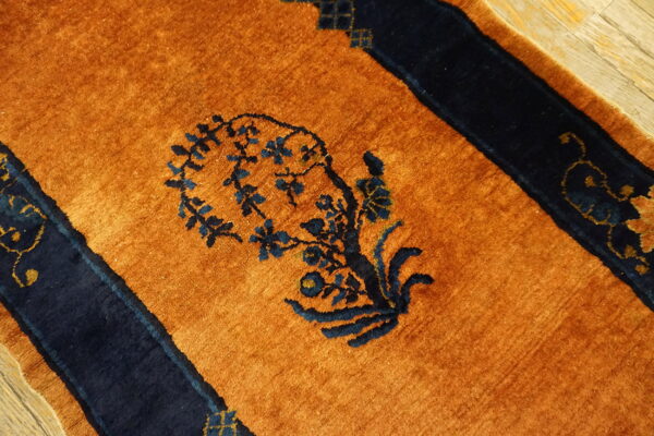 Orange rug with navy blue floral pattern and borders resting on light wood flooring.