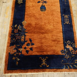 Rust orange rug with a navy blue border displaying floral and geometric patterns on worn hardwood.