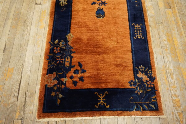 Rust orange rug with a navy blue border displaying floral and geometric patterns on worn hardwood.