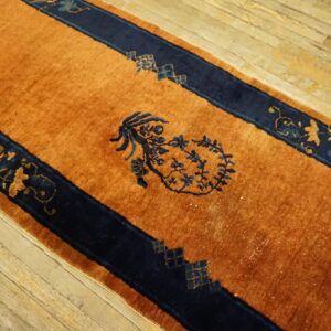 Rust-colored runner rug with navy blue striped borders and stylized floral details on worn wood planks.