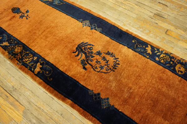 Rust-colored runner rug with navy blue striped borders and stylized floral details on worn wood planks.