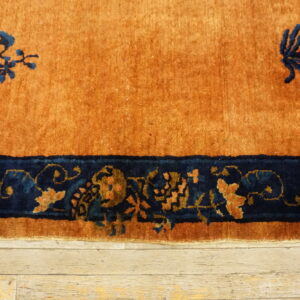 Rust rug featuring deep blue decorative motifs and a wide border rests on light wood flooring.