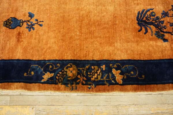 Rust rug featuring deep blue decorative motifs and a wide border rests on light wood flooring.