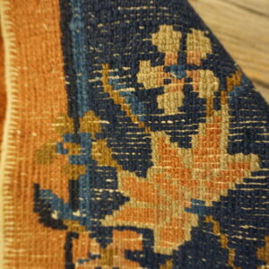 Close-up shows a folded navy blue and rust rug with geometric patterns on rough wooden flooring.