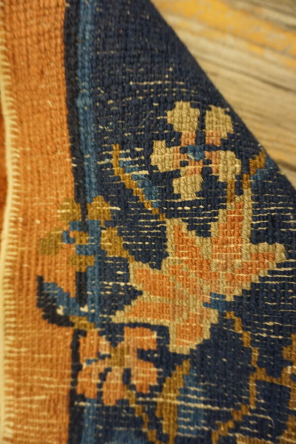 Close-up shows a folded navy blue and rust rug with geometric patterns on rough wooden flooring.