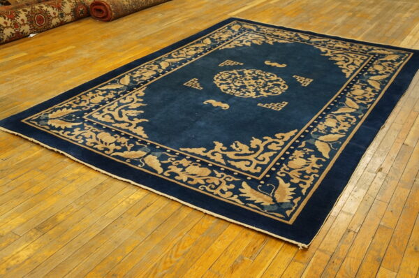 A rectangular blue rug with a light gold asian scroll pattern lies on a shiny wooden floor.