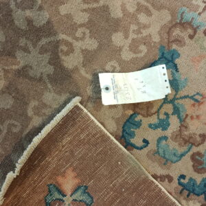 Close-up of a low-pile floral rug in muted brown, tan, and teal, with its woven backing exposed.