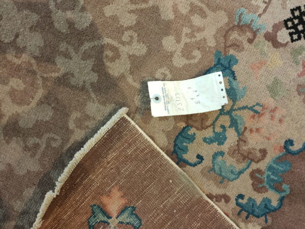 Close-up of a low-pile floral rug in muted brown, tan, and teal, with its woven backing exposed.