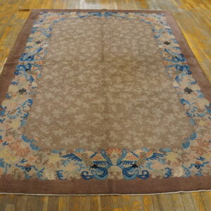 Traditional brown and tan rug featuring a tone-on-tone field and elaborate blue and peach border designs on wood floor.