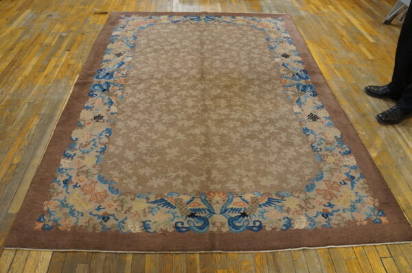 Traditional brown and tan rug featuring a tone-on-tone field and elaborate blue and peach border designs on wood floor.
