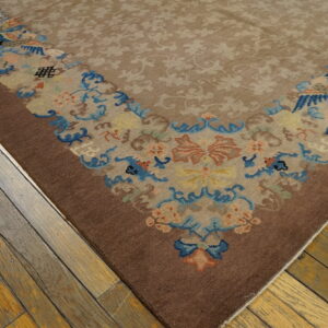 Beige and brown area rug with a multicolored floral border lying on worn wooden plank flooring.