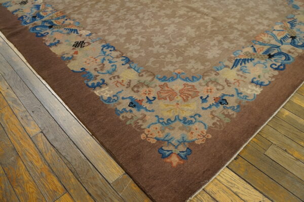 Beige and brown area rug with a multicolored floral border lying on worn wooden plank flooring.