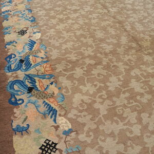 Close-up of a tan rug field with subtle tonal patterns bordered by rich blue, peach, and brown intricate designs.