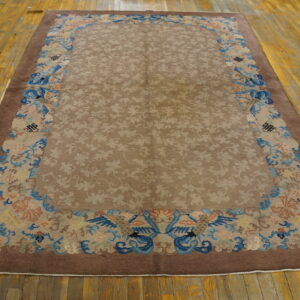 A brown rug with ornate blue and peach bird borders lies on a worn wooden floor beside black shoes.