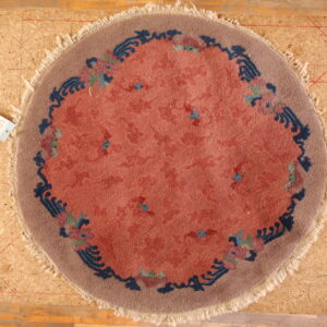 Round rug with a coral field and stylized blue, rose, and taupe floral border on an OSB board.