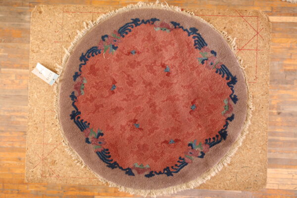 Round rug with a coral field and stylized blue, rose, and taupe floral border on an osb board.