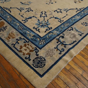 Corner view of a cream rug with blue and tan traditional patterns on a distressed hardwood floor.