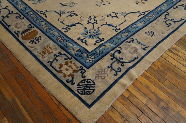 Corner view of a cream rug with blue and tan traditional patterns on a distressed hardwood floor.
