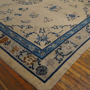 Cream and blue rug with thick pile and ornate border rests on wide distressed hardwood floorboards.