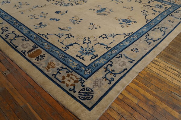 Cream and blue rug with thick pile and ornate border rests on wide distressed hardwood floorboards.