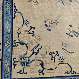Textured beige rug with a dark blue and light blue scrolling vine pattern near the wide light blue border.