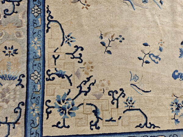 Textured beige rug with a dark blue and light blue scrolling vine pattern near the wide light blue border.