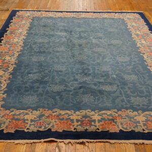 A blue rug with a tone-on-tone floral field and a wide coral, beige, and navy border rests on wood planks.